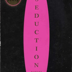 May include: A book cover for "The Art of Seduction" by Robert Greene. The cover features a black background with a vertical, elongated pink shape in the center. The title and author's name are in white text. A gold seal is in the upper left corner.