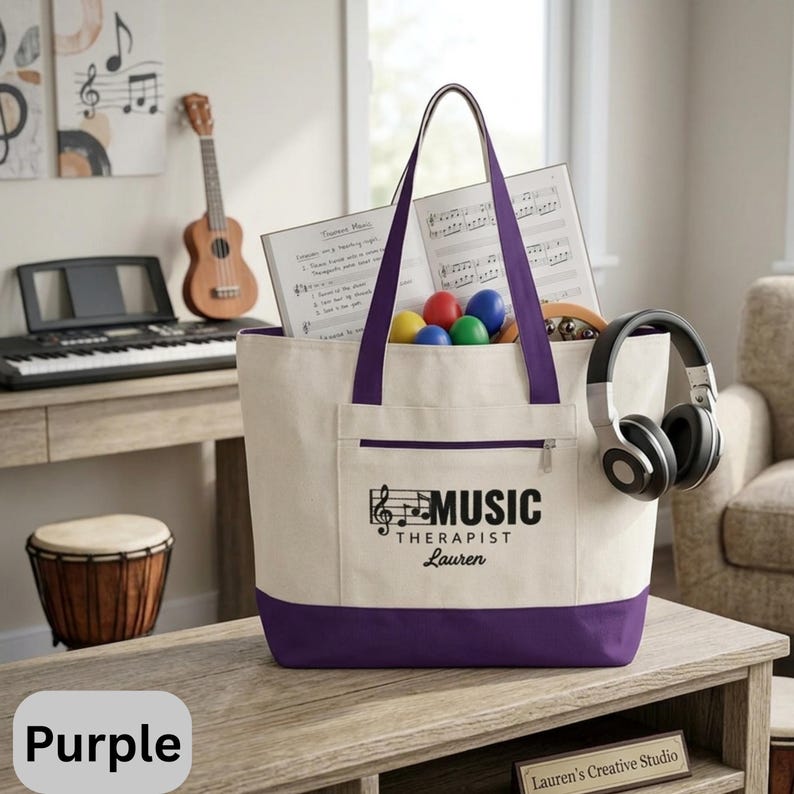 May include: A canvas tote bag with purple accents, featuring the text "MUSIC THERAPIST Lauren". The bag is filled with sheet music, colorful maracas, and a pair of headphones. A keyboard, ukulele, and drum are visible in the background.