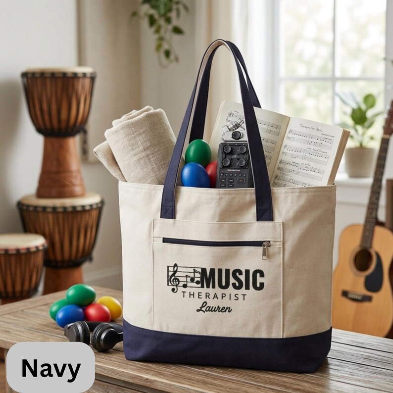 May include: A navy and cream tote bag with the text "MUSIC THERAPIST Lauren". The bag is filled with a beige blanket, colorful eggs, sheet music, and a small audio device. A pair of headphones and drums are in the background.