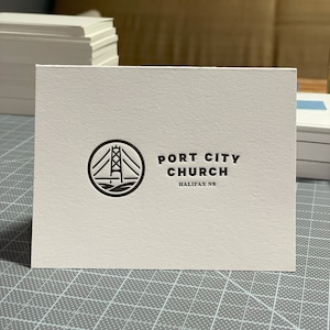May include: A white card with a black logo of a bridge in a circle and the text "PORT CITY CHURCH HALIFAX NS".