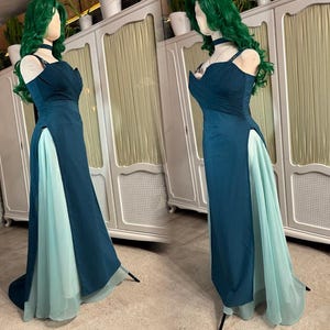 Puede incluir: Un vestido de fiesta de color verde azulado con una abertura alta que revela una capa inferior azul claro. El vestido presenta un escote coraz&oacute;n y tirantes finos. El vestido se exhibe en un maniqu&iacute; con una peluca verde y gargantilla.