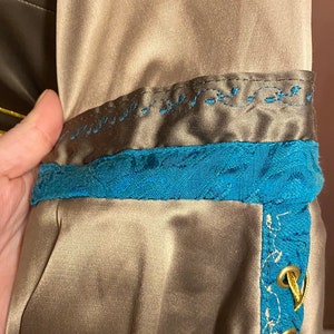 May include: A brown satin fabric with a blue and gold trim. The trim has a decorative pattern and gold eyelets with a gold cord threaded through them.