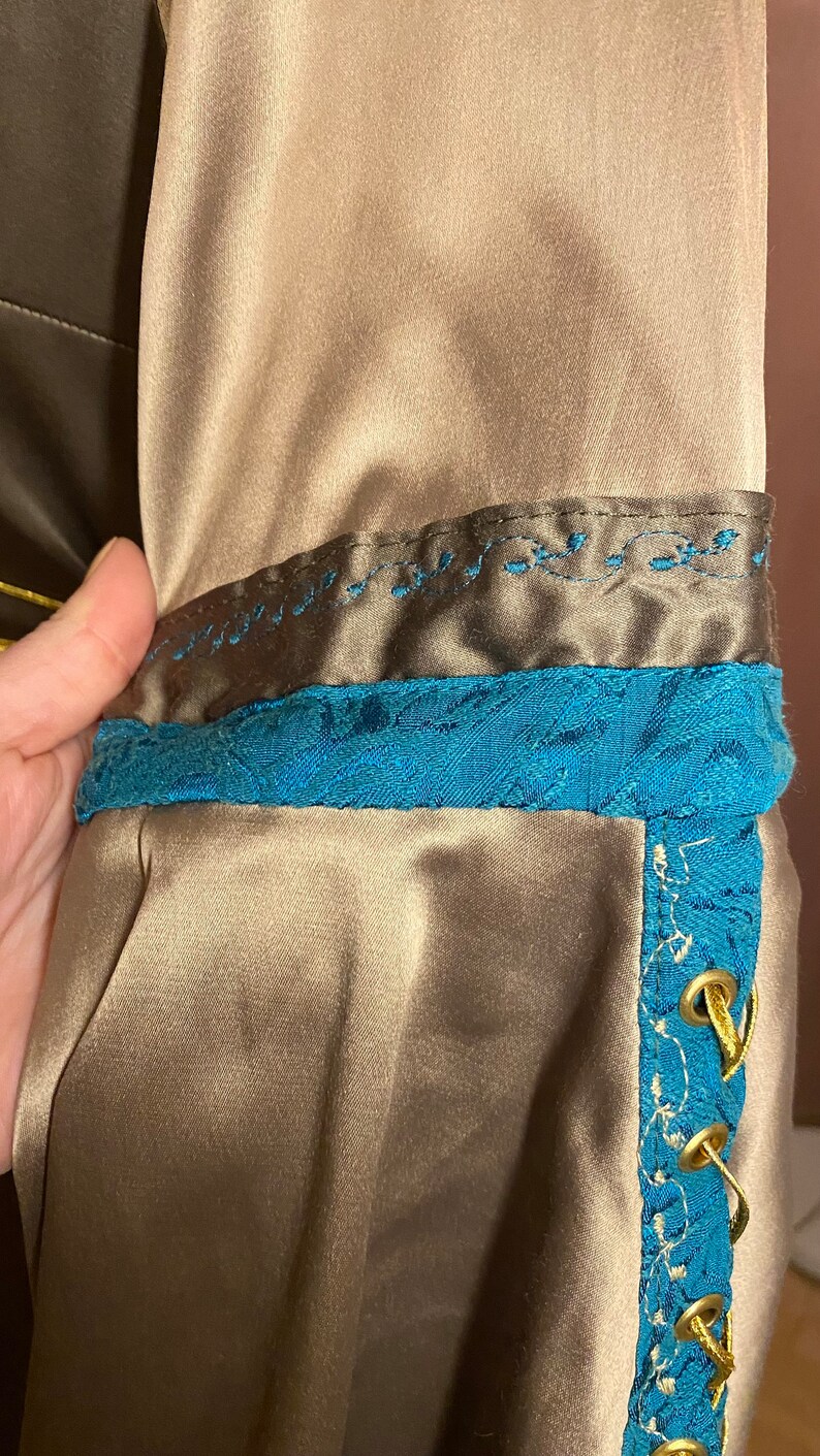 May include: A brown satin fabric with a blue and gold trim. The trim has a decorative pattern and gold eyelets with a gold cord threaded through them.