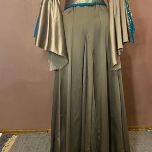 May include: A long, flowing, brown dress with a teal and gold trim. The dress has a V-neckline and long sleeves with a bell shape. The dress has a belt at the waist.