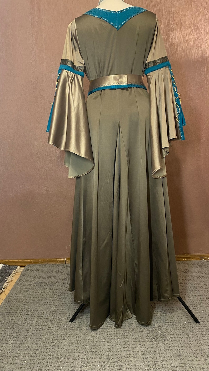 May include: A long, flowing, brown dress with a teal and gold trim. The dress has a V-neckline and long sleeves with a bell shape. The dress has a belt at the waist.