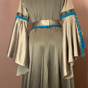May include: A long, flowing gown with a teal and gold trim. The gown has a V-neckline and a fitted bodice. The sleeves are long and wide, with a gathered cuff. The gown is made of a soft, silky fabric.