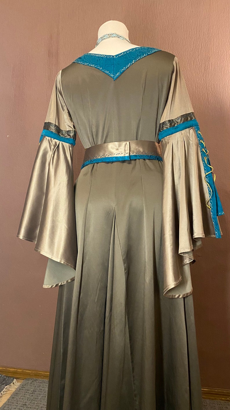 May include: A long, flowing gown with a teal and gold trim. The gown has a V-neckline and a fitted bodice. The sleeves are long and wide, with a gathered cuff. The gown is made of a soft, silky fabric.