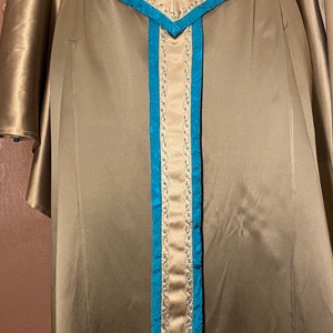 May include: A long, flowing, brown satin dress with a teal blue trim. The dress has a V-shaped neckline and a long, pointed belt with a teal blue trim.