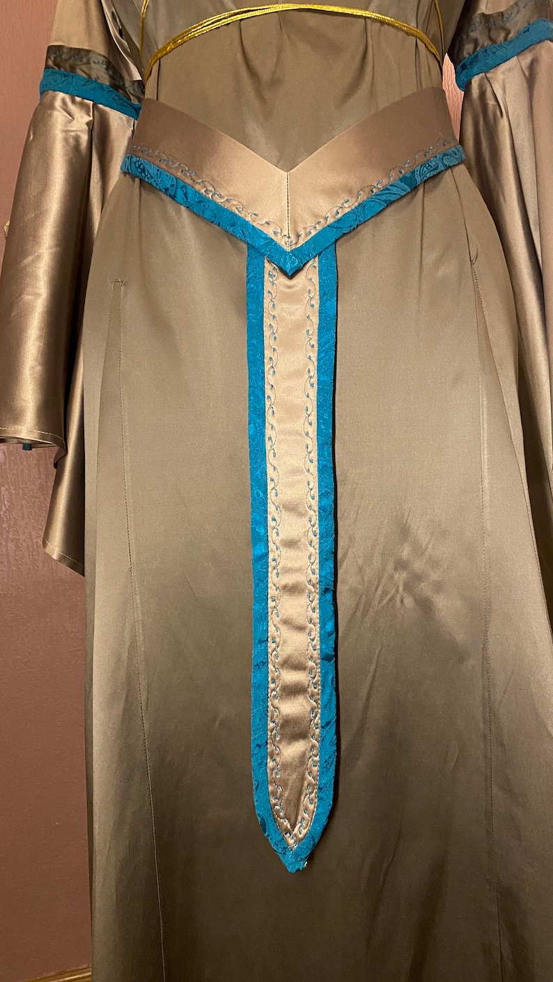 May include: A long, flowing, brown satin dress with a teal blue trim. The dress has a V-shaped neckline and a long, pointed belt with a teal blue trim.