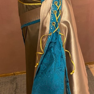 May include: A long-sleeved dress with a brown bodice and a beige skirt. The sleeves have a blue and gold lace-up detail.