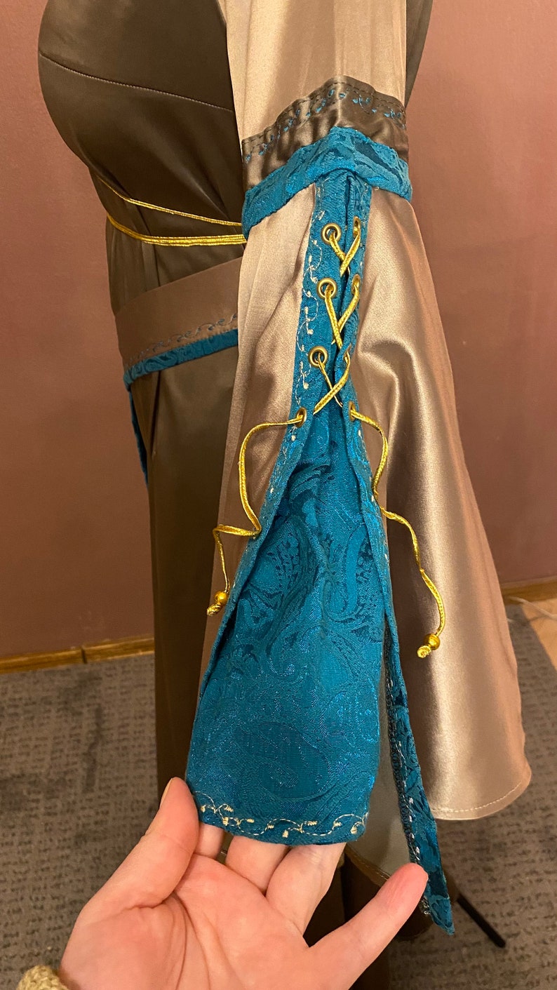 May include: A long-sleeved dress with a brown bodice and a beige skirt. The sleeves have a blue and gold lace-up detail.