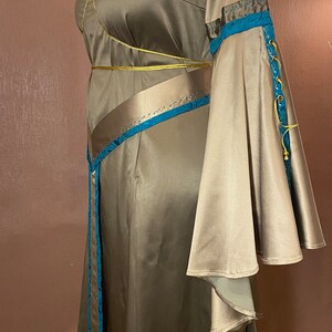 May include: A long, flowing brown satin dress with a blue and gold trim. The dress has a fitted bodice and a flowing skirt. The sleeves are long and bell-shaped.