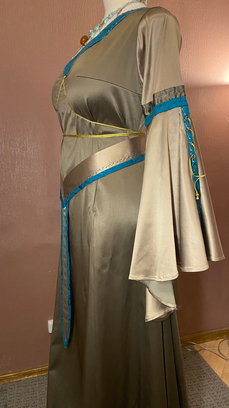 May include: A long, flowing brown satin dress with a blue and gold trim. The dress has a fitted bodice and a flowing skirt. The sleeves are long and bell-shaped.