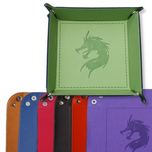May include: A set of six dice trays featuring a dragon design. The trays are made from felt and come in a range of colours, including green, purple, blue, red, black, and brown.