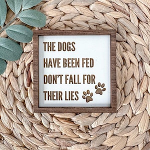 May include: A wooden sign with the text "The dogs have been fed don't fall for their lies" and two paw prints.