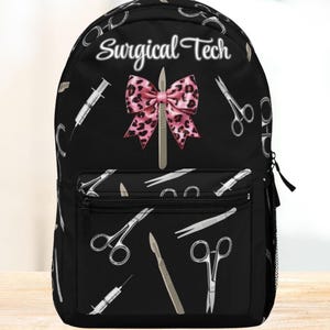 Puede incluir: Mochila negra con un patrón de instrumentos quirúrgicos, tijeras, jeringas y bisturíes. La mochila presenta el texto "Surgical Tech" y un lazo rosa con estampado de leopardo. Una bolsa práctica y elegante para profesionales médicos.