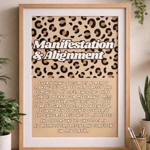 Puede incluir: Un cartel enmarcado con las palabras "Manifestation & Alignment" en una fuente elegante, sobre un fondo de estampado de leopardo. El cartel incluye un mensaje inspirador. El marco es de color marrón claro y el cartel se muestra en un escritorio de madera.