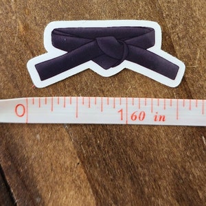 May include: Black martial arts belt sticker. The belt is tied in a knot and is about 1.6 inches wide.