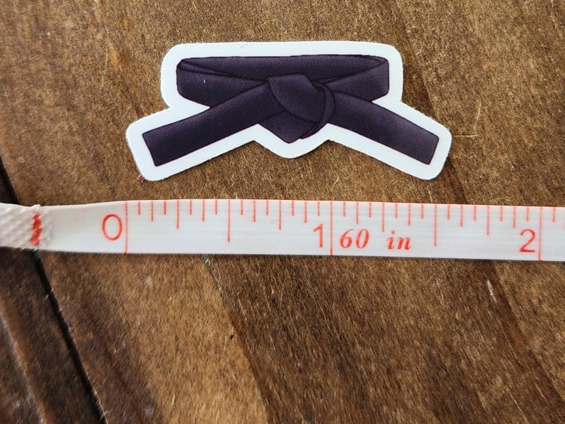 May include: Black martial arts belt sticker. The belt is tied in a knot and is about 1.6 inches wide.