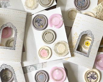 May include: Assortment of wax seals with floral and geometric designs. The seals are in various colors, including pink, white, and brown. The seals are arranged on a white background.