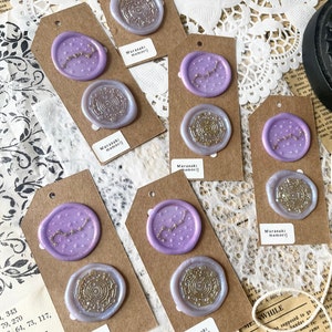 May include: Six purple wax seals with gold accents on brown card stock tags. The seals feature a constellation design and a circular design. The tags have the text "Murasaki memori" printed on them.