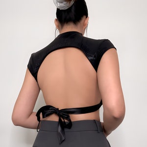 May include: Black crop top with a keyhole back and a black satin ribbon tie at the back.