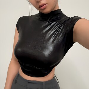 May include: A black, shiny, mock neck shirt with short sleeves. The shirt is cropped and has a fitted silhouette.