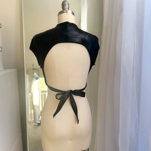 May include: A black satin crop top with a low back and a tie closure. The top is on a white mannequin.