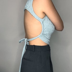 May include: A light blue sleeveless top with a cutout back and a tie closure at the back. The top is made of a soft, textured fabric.
