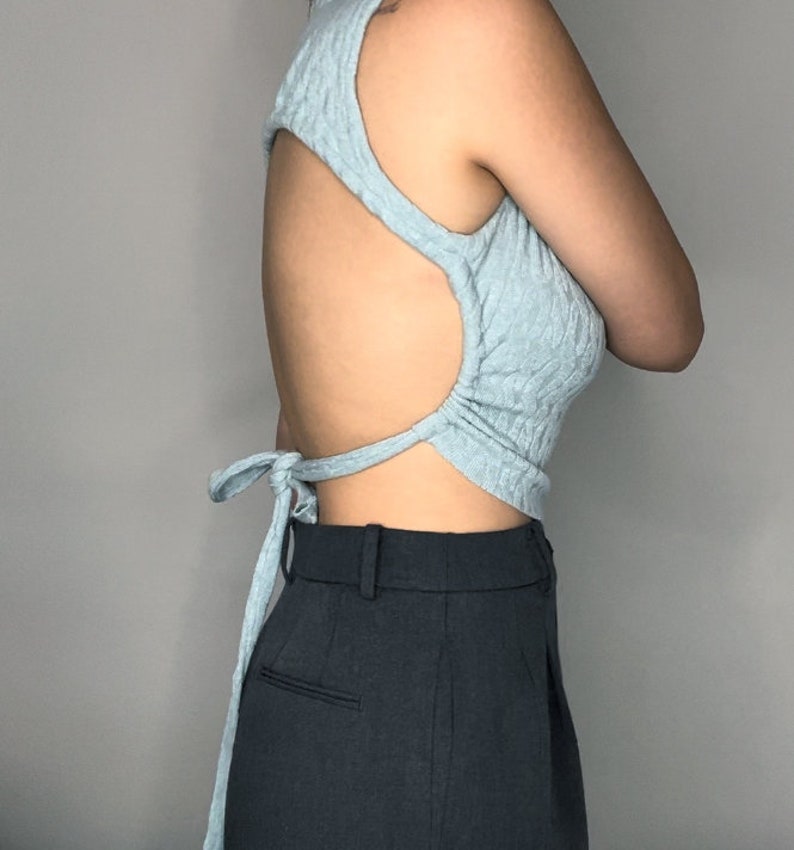 May include: A light blue sleeveless top with a cutout back and a tie closure at the back. The top is made of a soft, textured fabric.