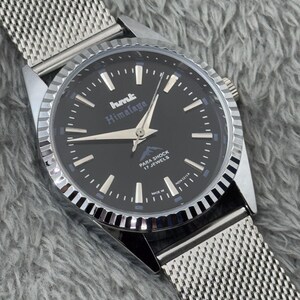 Puede incluir: Un reloj de pulsera plateado con esfera negra y correa de malla. La esfera del reloj presenta marcadores de hora y agujas blancas, y el texto "hmt Himalaya". El reloj tambi&eacute;n tiene el texto "PARA SHOCK 17 JEWELS".