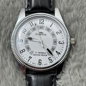 K&ouml;nnte beinhalten: Silberfarbene Fortis-Uhr mit wei&szlig;em Zifferblatt, schwarzen Zeigern und schwarzem Lederarmband. Das Zifferblatt zeigt das Fortis-Logo, die Aufschrift "17 Jewels Shock Proof" und die Zahlen 1 bis 12. Die Uhr hat eine strukturierte L&uuml;nette.