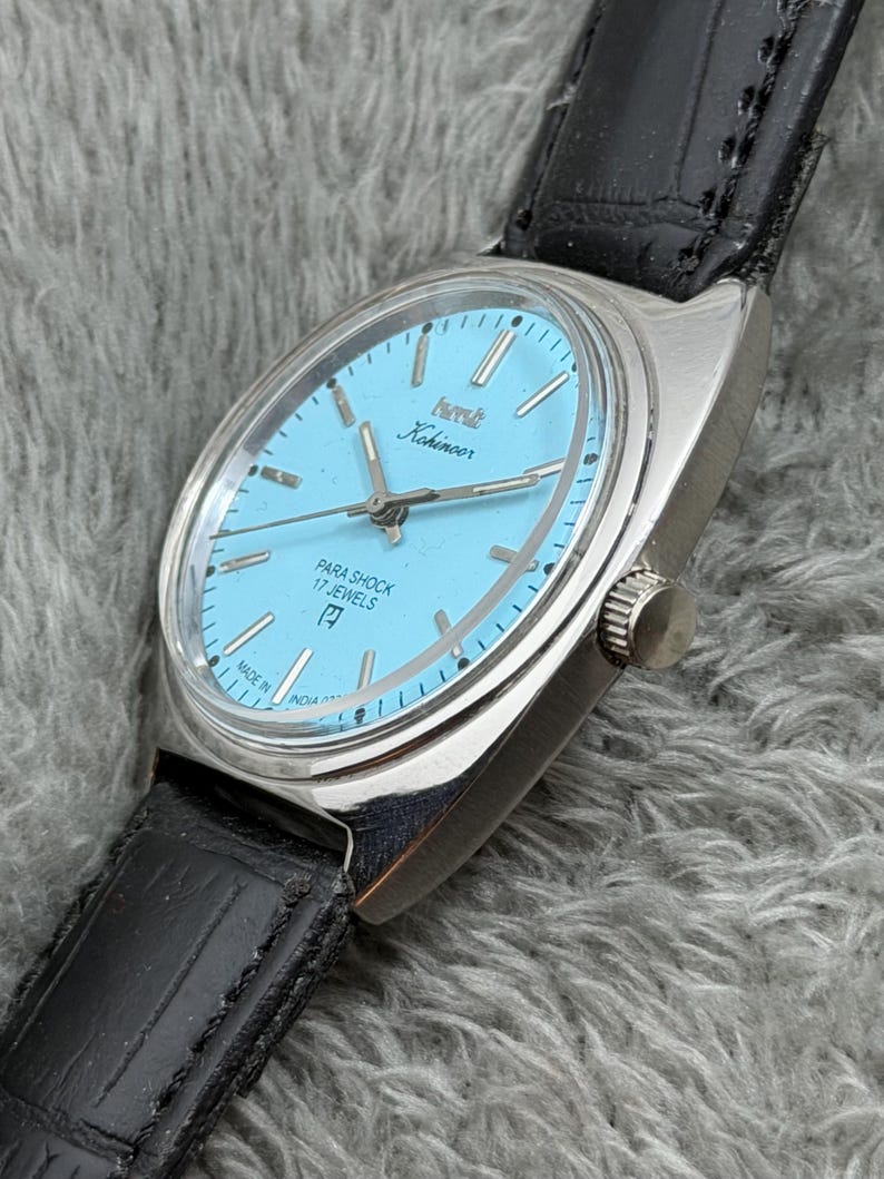 May include: A vintage Kohinoor wristwatch with a light blue face and silver case. The watch features a black leather band and the text "PARA SHOCK 17 JEWELS". The watch is marked "MADE IN INDIA".