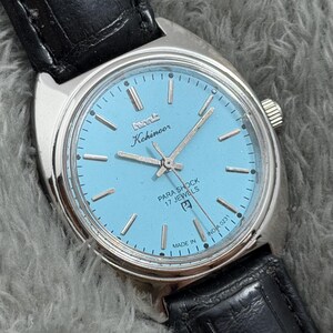 May include: A vintage Kohinoor Para Shock watch with a light blue face and silver hands and markers. The watch has a stainless steel case and a black leather strap. The watch face includes the text "PARA SHOCK 17 JEWELS" and "MADE IN INDIA 0231".