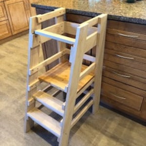 May include: A wooden step stool with a platform and steps for children to reach higher surfaces. The stool is made of natural wood and has a simple design.