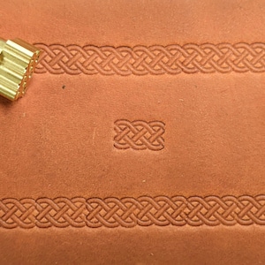 May include: A close-up of a leather stamping tool featuring a Celtic knot design. The tool is made of brass and has a wooden handle. The tool is used to create decorative patterns on leather.