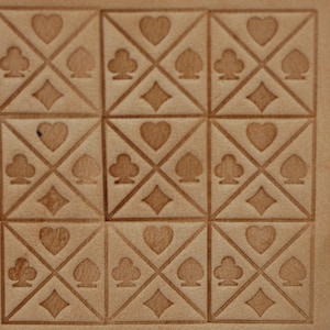 Può includere: Primo piano di una superficie in pelle marrone chiaro con un motivo ripetuto di semi di carte da gioco. Ogni quadrato presenta un design a cuore, picche, fiori e quadri. Il motivo in rilievo è un elemento decorativo.