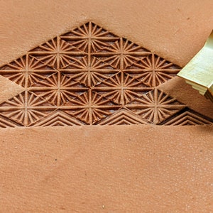 May include: A brass leather stamping tool with a geometric pattern. The tool is used to create a decorative design on leather.