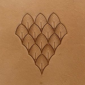 May include: Close-up of a tan leather surface with a carved, symmetrical design. The design features a series of layered, fan-shaped elements, creating a textured, decorative pattern. The overall aesthetic is natural and earthy.