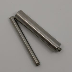 May include: Two cylindrical metal components with a smooth, brushed silver finish. Each piece features a threaded end, allowing for connection. The objects are positioned diagonally, showcasing their metallic texture and simple, functional design.