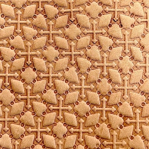 May include: A close-up of a textured leather surface with a repeating pattern of embossed crosses and diamonds. The leather is a light brown colour.