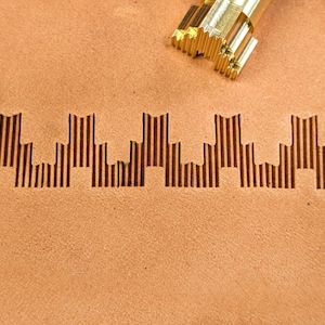 May include: A close-up of a leather surface with a decorative pattern embossed into it. The pattern is a series of vertical lines that create a cityscape effect.