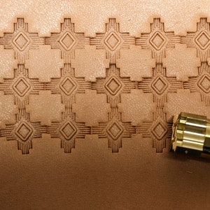 May include: A close-up of a leather stamping tool with a geometric design. The tool is being used to create a repeating pattern on a piece of brown leather.