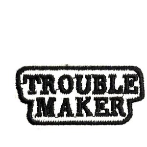 May include: Embroidered patch with the words "TROUBLE MAKER" in black, outlined in a black border. The patch has a textured appearance and is set against a white background. Ideal for jackets, bags, or other fabric items.
