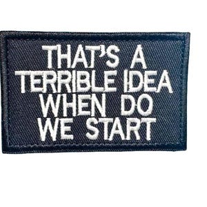 May include: A rectangular black patch with white embroidered text that reads "THAT'S A TERRIBLE IDEA WHEN DO WE START". The patch has a black border and is likely designed to be sewn or ironed onto clothing or accessories.