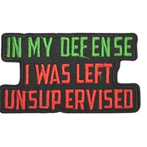 May include: Black embroidered patch with the text "IN MY DEFENSE I WAS LEFT UNSUPERVISED" in green and red lettering. The patch has a rectangular shape with a unique design.