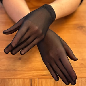 Puede incluir: Un par de guantes negros transparentes. Los guantes están hechos de una tela delicada y transparente, con una apariencia ligeramente texturizada. Los guantes tienen un diseño ajustado, que cubre las manos y las muñecas.
