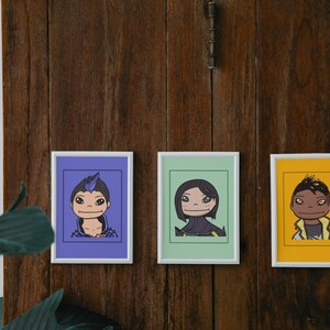 May include: Three framed illustrations of cartoon characters. The first character has blue hair and is wearing a purple shirt. The second character has black hair and is wearing a green shirt. The third character has brown skin and is wearing a yellow shirt.