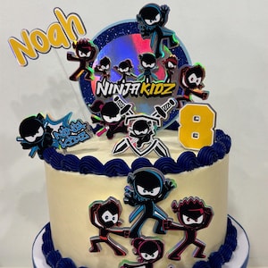 Puede incluir: Tarta redonda con glaseado amarillo claro, decorada con remolinos de glaseado azul y adornos con temática ninja. La tarta presenta el nombre "Noah" y el número "8". El logotipo de Ninja Kidz también es visible.