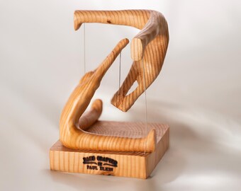 May include: A wooden sculpture of two figures in a dynamic pose, crafted from natural wood with visible grain. The sculpture is mounted on a square wooden base with the inscription "HAND CRAFTED BY PAUL KLEIN".
